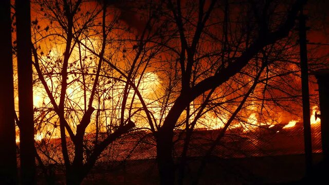 fire on the roof of the house. a burning at night trees building house close-up. home insurance apartment concept. huge fire blazes houses and trees. property 911 damage arson protection