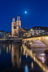 Fototapeta na wymiar Munsterbrucke and Grossmunster church reflecting in the blue hour in river Limmat, Zurich, Switzerland