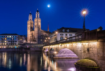 Fototapeta na wymiar Munsterbrucke and Grossmunster church reflecting in the blue hour in river Limmat, Zurich, Switzerland