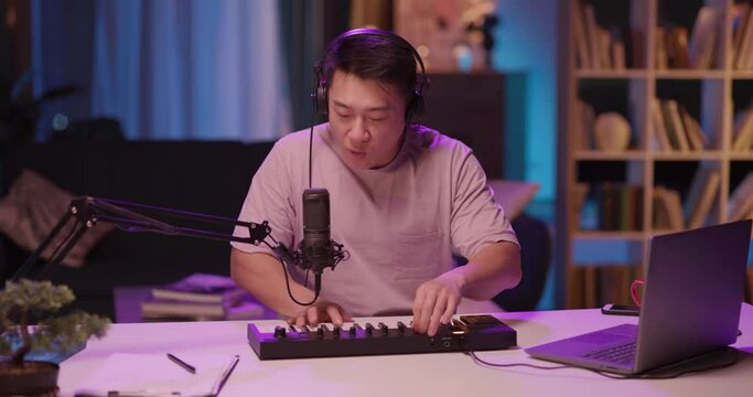 Inspired Asian Male Artist Singing into Microphone Recording Electronic Audiotrack on Piano Synthesizer Enjoying Staying Home Late at Midnight.