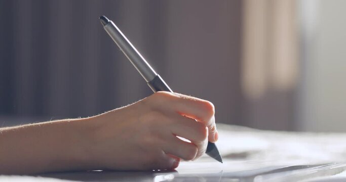 Close up view of woman hand using digital tablet drawing with stylus pen. Designer working on bed at home.