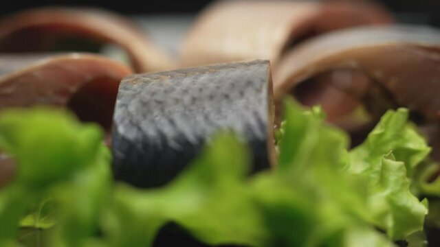 Close up herring in chunks with greens are rotating on the plate on black background. Healthy food clean eating selection.