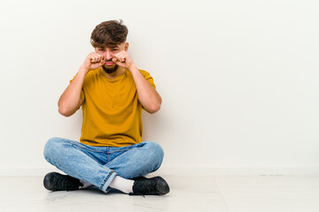 Young Moroccan man sitting on the floor isolated on white background whining and crying disconsolately.
