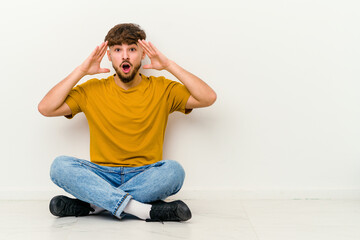 Young Moroccan man sitting on the floor isolated on white background celebrating a victory or success, he is surprised and shocked.