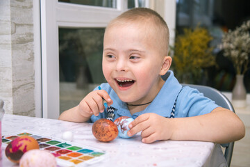 A boy with Down syndrome draws, a genetically ill child paints Easter eggs, preparation for Easter,...