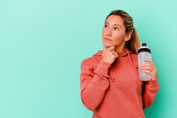Young caucasian sport woman drinking water isolated on blue backgroundlooking sideways with doubtful and skeptical expression.
