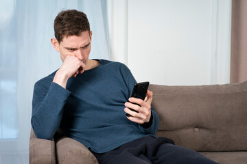 Portrait of sad upset angry guy, serious frustrated young man looking at screen of his cell mobile...