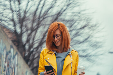 Woman using smartphone and drinking coffee outside