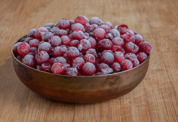 Frozen cranberries in a small copper bowl on a wooden background. Berries in an old vintage dish.