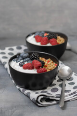 Muesli with yougurt and fresh berries in black bowl on dark gray background.