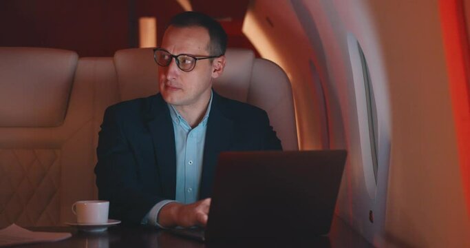 Flight attendant serving coffee for businessman working on laptop in first class