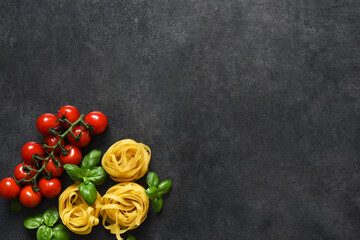 Ingredients for the pasta. Tagliatelle pasta, tomatoes and basil on a black concrete background.