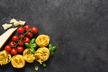 Tagliatele pasta, tomatoes, basil and parmesan cheese on a black concrete background. Ingredients for pasta with text space. Layout.