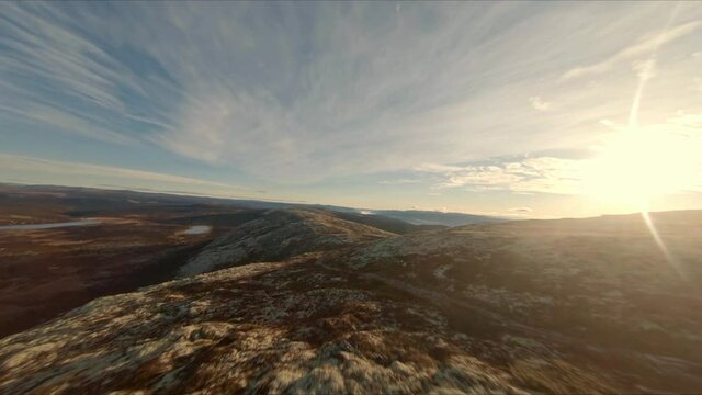 FPV drone flight over mountain ridge with sunset in the background and blue sky with a few clouds