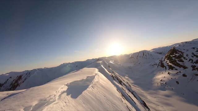 Spectacular fpv drone areal shot flight along a high mountain ridge covered in snow with view towards the sun geiranger valley in the far, and blue sky epic