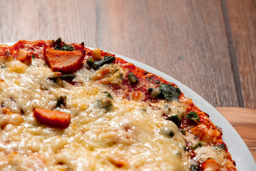 Cooked pizza with cheese and chicken pieces. Close up. Italian style meal. Fast food product on a wooden table surface.