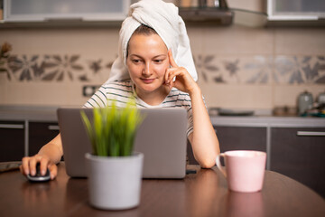 Woman with towel on hair working remotely at home using laptop