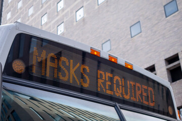 the front top of a city bus with a lighted sign reading Masks Required corona virus