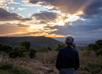 MALE FIGURE LOOKING AT THE SUNSET PANORAMA IN HILL LANDSCAPE