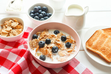 Tasty breakfast of whole wheat flakes with milk, blueberries and toasts close-up on wooden table. Concept of diet and healthy food. Selective focus