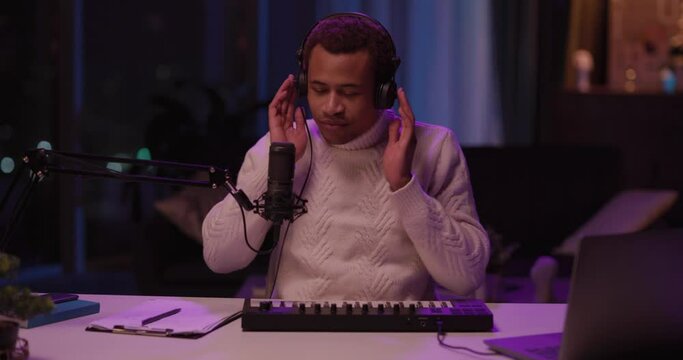 African american casual handsome guy recording audiotrack videoblogging and singing into microphone staying home at night.