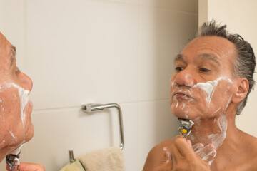 Senior man in the bathroom with shaving cream on his face shaving
