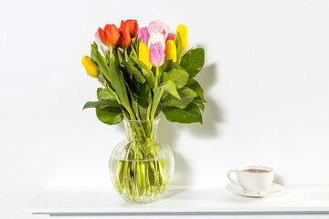 A bouquet of multi-colored tulips in a transparent vase and cup of tea