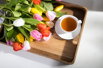 A bouquet of multicolored tulips and a cup of tea are on a tray on the table