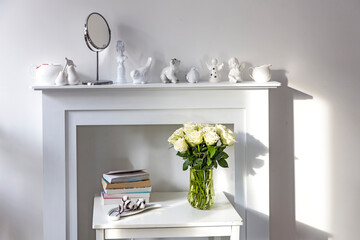 Bouquet of white roses in a glass figured vase on a white fireplace console.