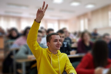 The student raises his hands asking a question in class in college