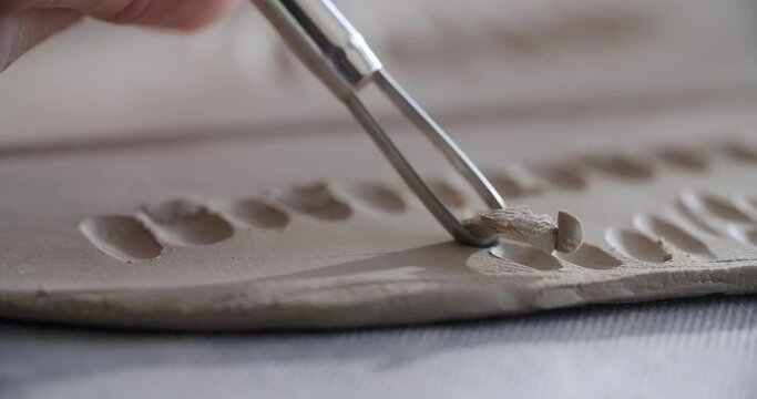 Close up view: potter carves a pattern on a raw clay, ceramist makes texured clay surface, making the ceramics at the pottery workshop, 4k 60p Prores HQ 10 bit