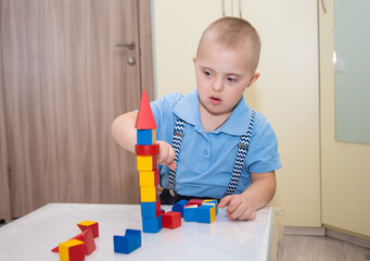 A boy with Down syndrome plays a construction set, a genetically ill disabled child builds a tower...