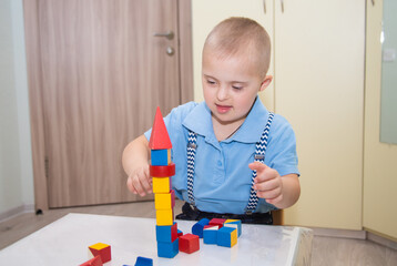 A boy with Down syndrome plays a construction set, a genetically ill disabled child builds a tower...