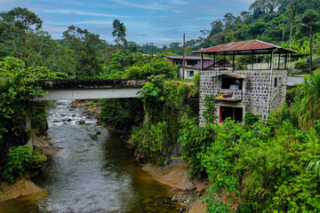 Fototapeta premium A stone house with a tin roof standing next to a bridge and a small stream