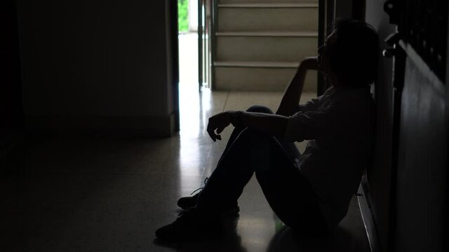 Silhouette of a stressed Troubled mansitting in the dark leaning against drinking beer sitting on steps the wall in old condo, lost in life.