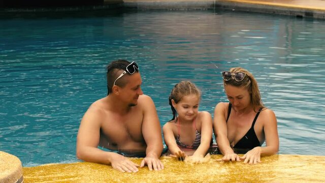 The mother and father with little daughter have fun in the pool. Mom and dad plays with the child. The family enjoy summer vacation in a swimming.