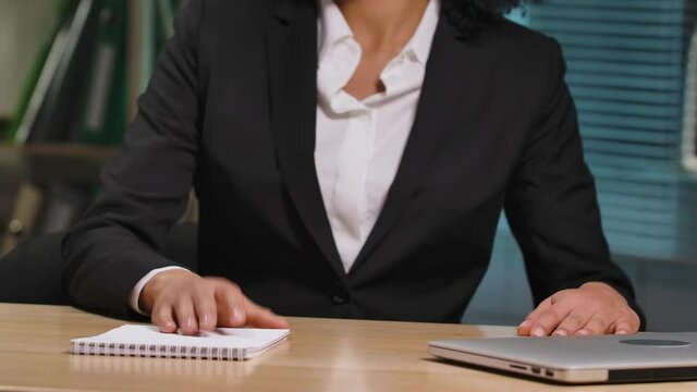 Portrait of African American woman sits down at the table, opens the laptop and starts work. Businesswoman posing at workplace, in interior of office. Close up. Slow motion ready 59.94fps.