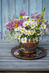 Obraz na płótnie Canvas A bouquet of wildflowers with daisies in a flowerpot on an old wooden table
