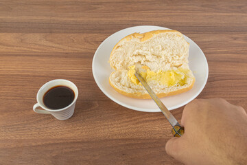 Brazilian Wheat Baked French Bread and coffee, on wooden table and buttering bread - perspective view.