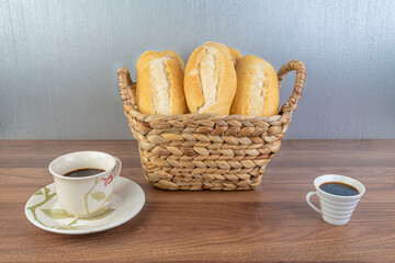 Brazilian Wheat Baked French Bread and two coffee, in straw basket on wooden table and gray background - perspective view.