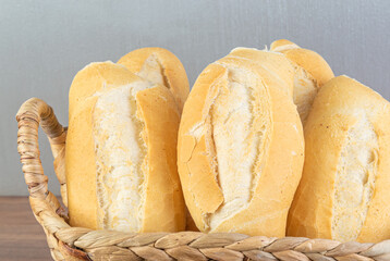 Brazilian Wheat Baked French Bread, in straw basket on wooden table and gray background - close view.