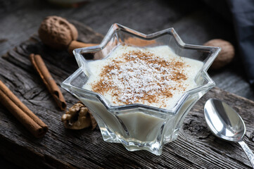 Pudding in glass bowl with cinnamon and walnut on rustic table, milk dessert