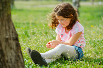 beautiful girl sits near tree and holds first spring flower. girl tore off plant Capsella bursa-pastoris. Collecting medicinal plants in spring.