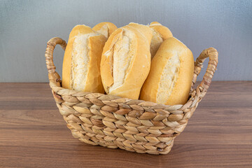 Brazilian Wheat Baked French Bread, in straw basket on wooden table and gray background - perspective view.