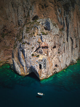 Aerial view of a small boat anchored in front of Porto Flavia touristic attraction facing the Mediterranean Sea, Sardinia, Italy.