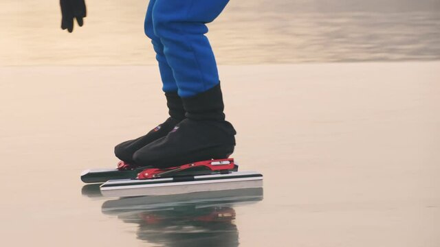 The child train on ice speed skating. The legs in skates close up. The kid girl skates in the winter in sportswear sport glasses. Outdoor slow motion.