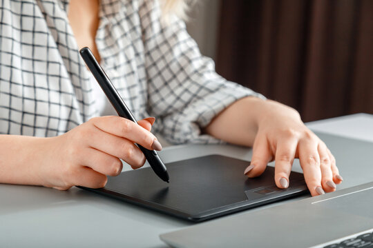 Closeup woman designer editor or photographer use graphics tablet laptop at home office workplace. Creative designer working with professional equipment. Stylus in hand draws on graphics tablet.