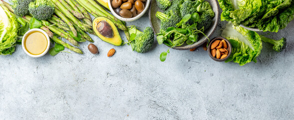 Vegetarian green ingredients on gray background. Vegetarian food - vegetables, greens, avocado, oil - health or cooking concept. Background layout with free text space