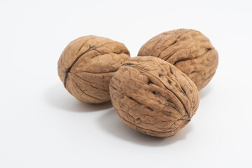 Vista de cerca de tres nueces, frutos del nogal (Juglans regia), de color marrón y textura rugosa, aisladas sobre fondo blanco.