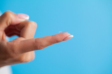 Young woman holding contact lens on finger.